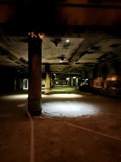 A very grungy abandoned mall concourse with some of the lights still on. It gives off an extremely creepy vibe