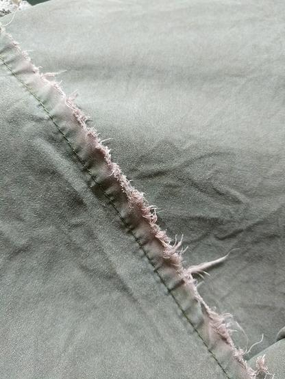 A ragged hem on a muted green garment. The hem is pale pink.