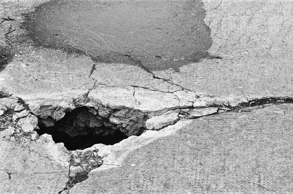 A grainy black and white photograph showing where an extended crack in the pier has opened into a deep, dark hole, dangerous to ankles and small dogs.