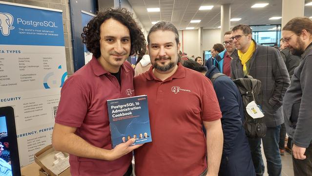 Boriss Mejias and Jimmy Angelakos at the PostgreSQL Europe booth, signing the PostgreSQL 16 Administration Cookbook