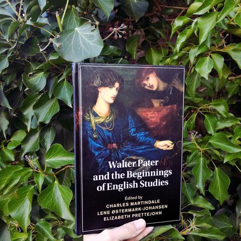 Holding the essay collection Walter Pater and the Beginnings of English Studies in front of a bush