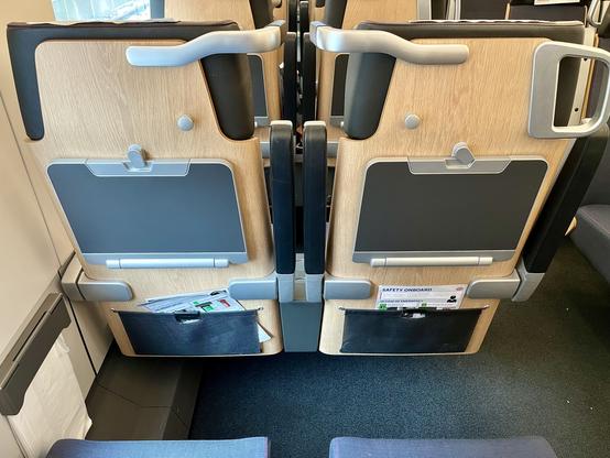 Rückseite von Zweiersitzen. Ausgekleidet mit Holz und Aluminiumelementen. Kopfstütze aus Leder oder Lederimitat. Unten eine elastische Tasche mit Heftchen, mittig Klapptischchen, oberhalb davon jeweils zur Mitte der Zweiersitze sind Kleiderhaken. Am Gang oben ein Haltegriff. Zwischen den zwei Sitzen zwei komische Griffe, die Leselampen sind. An der Wand die im Norden üblichen Mülltüten, hier jedoch mit stylischer Abdeckung.