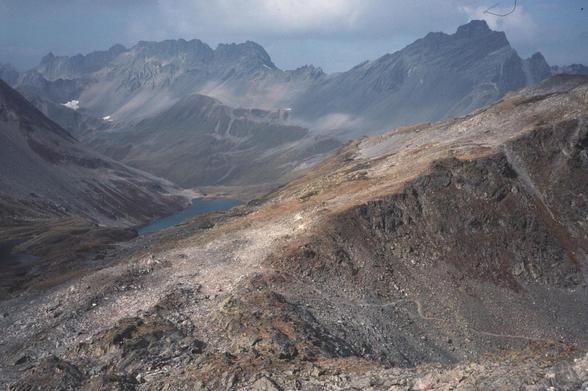Looking down on a pass over a high rocky ridge. There is a sharp toothed ridge in the background made of dark rock against a dark sky