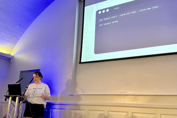 Pauline Vos giving a presentation next to a projected screen displaying command line instructions.