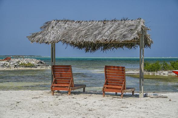Two wooden reclining chairs under a thatched sun roof on the beach at the caribbean ocean in Bonaire