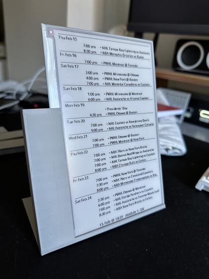 A bare epaper glass display with a list of upcoming sports games on it. It’s held at a 20% angle to the vertical with a grey plastic printed part that holds the display on the bottom and left sides