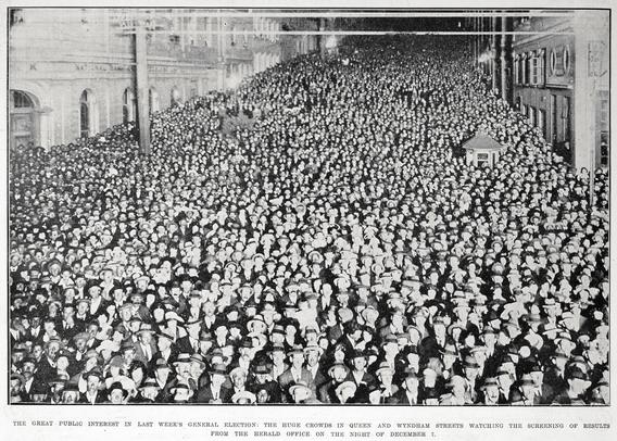 Black-and-white photo: The great public interest in last week’s general election. The huge crowds in Queen and Wyndham streets watching the screening of results from the Herald office on the night of December 7. Description: a night-time photo of an upward sloping street packed with a crowd of men and women, formally dressed and wearing hats. Citation: Auckland Weekly News, 14 December 1922, p. 38. Auckland Libraries Heritage Collections AWNS-19221214-38-01. https://kura.aucklandlibraries.govt.nz/digital/collection/photos/id/238277