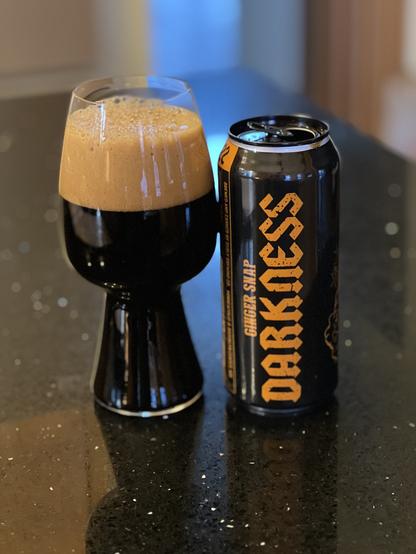 A black pint can of 2022 Surly Brewing Ginger snap Darkness. The can has cold orange lettering. A glass of beer has a tall tan head.