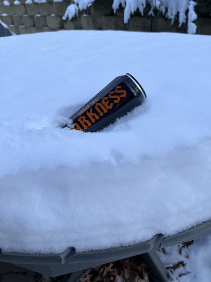 A pint can of Surly Darkness lays on 6 inches of snow on a picnic table.