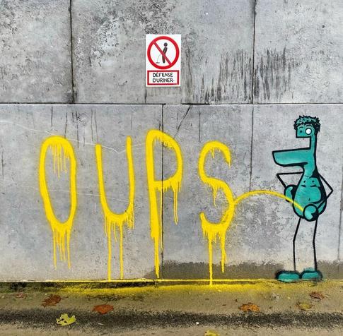 Streetartwall. A funny comic-style mural has been spray-painted on a gray concrete wall with a sign against urinating on it. It is a simply drawn, naked, green male with a protruding lower jaw, one large and one small eye, flat curls, thin arms and legs and round hands and feet. He stands cheerfully against the wall and pees the yellow letters "Oups" in a high arc on the wall. The white and red warning plaque with a crossed-out black pictogram hangs (also painted) above it: a little man peeing and the words "Urination defense" in French. He must not have seen it. 😉
