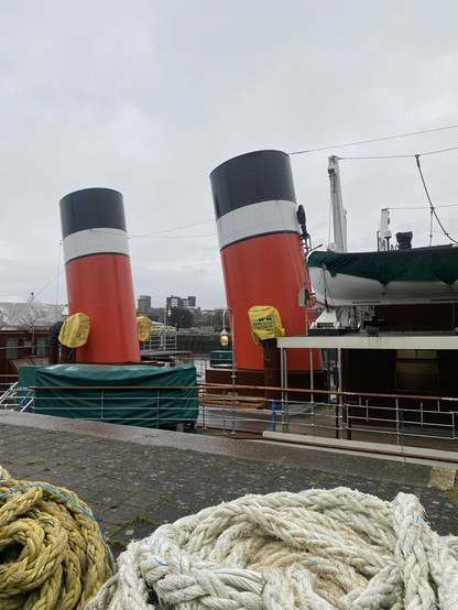 The two distinctive raking red white and black funnels of the paddlesteamer at the quayside.