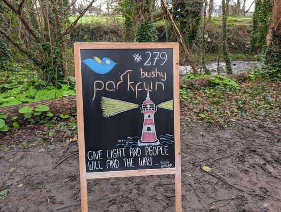 Sandwich board saying Bushy Parkrun number 279 with a chalk drawing of a lighthouse and the words: Give light and people will find the way (Ella Baker)