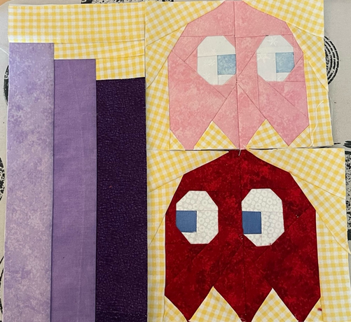 Paper Piecing Block. Link sind drei Lila Bücher, die in der Farbintensität zu nehmen und dabei immer kleiner werden, rechts sind ein rosa und ein roter Geist aus Packman übereinander. Der Rote blickt auf die lila Bücher, der Rosane aus dem Block raus.
