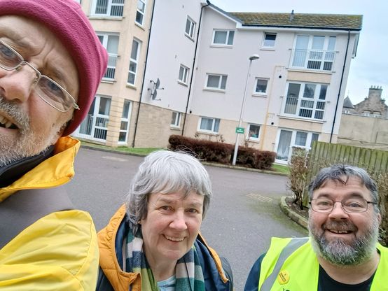 Selfie of three activists about to go canvassing in Nairn with flats shown behind being the target