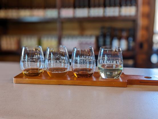 Four taster glasses on a board. All have reasonably clear liquid. Four are meads, one is wine.