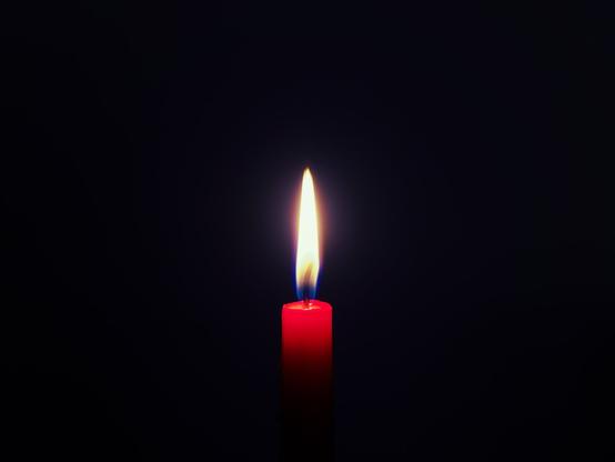A slim, burning red candle against a dark background.