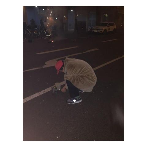 Foto zeigt einen Mann von hinten. Er hockt auf einer Straße und ist im Begriff, eine Böllerbatterie anzuzünden.