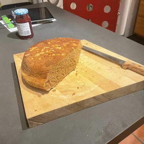 A freshly baked loaf of whole wheat bread on a cutting board w/ bread knife.