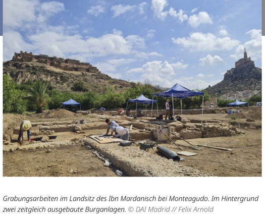 Foto der Ausgrabungsarbeiten im Landsitz des Ibn Mardanisch bei Monteagudo; zu sehen sind Grabungsflächen, über denen z.T. einige Sonnendächer errichtet sind. Im Hintergrund thronen zwei Burganlagen auf einer Erhebung.