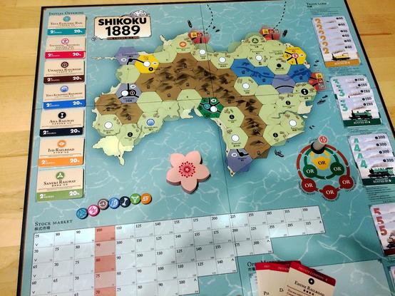 the Shikoku 1889 game board showing the hex map, initial offering shares, stock market chart, some tokens, etc.