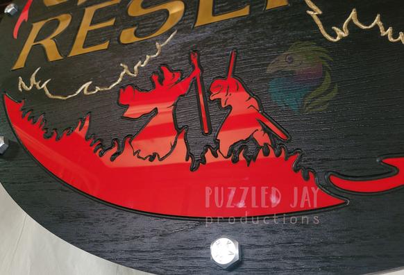 a round sign, with gold text and red images on a black background, depicting a dragon fighting a knight & wizard. Text reads "the game reserve"