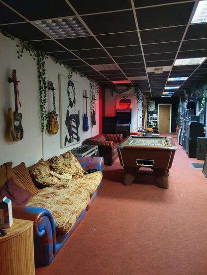 Long room with guitars on the walls, a pool table, a pin ball machine against a wall, red carpets, comfy sofa. Bliss.