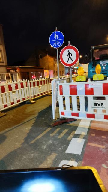Foto einer Baustelle auf dem Gehweg. Die daneben liegende Fahrspur ist gesperrt und gleichzeitig mit den Verkehrszeichen "gemeinsamer Fuß- und Radweg" sowie " Verbot für Fußgänger" beschildert