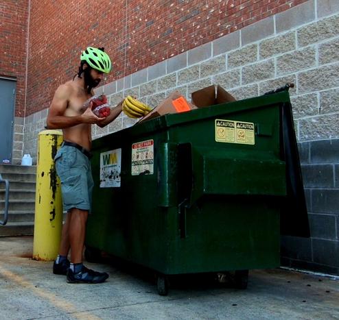 Daniel Troia—shirtless and wearing shorts, shoes, and a bicycle helmet—stands alongside a dumpster. His “dumpster diving” has resulted in finding bananas and other still edible food. 

Photo provided to Bicycling Monterey courtesy of Daniel Troia.