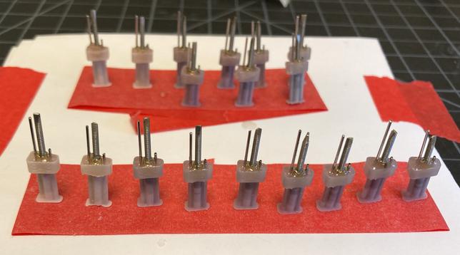 Photo of the shuttle “assembly line”: 9 shuttle molds with their inserted cannulas and rods and filled with dental cement. They are placed on a strip of red tape.