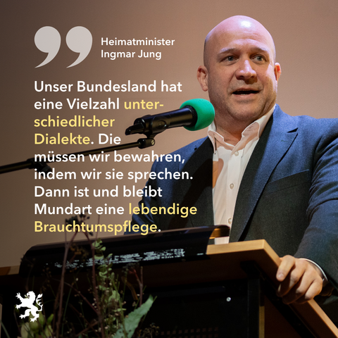 Bild: Heimat Minister Ingmar Jung am Rednerpult. Text: Unser Bundesland hat  eine Vielzahl unter schiedlicher  Dialekte. Die  müssen wir bewahren,  indem wir sie sprechen.  Dann ist und bleibt  Mundart eine lebendige Brauchtumspflege.