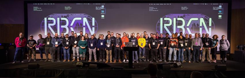 All speakers on stage at the end of Robocon Helsinki.

Spotlights in the speakers that gather for a group picture. 2 big screens in the back show "RBCN"