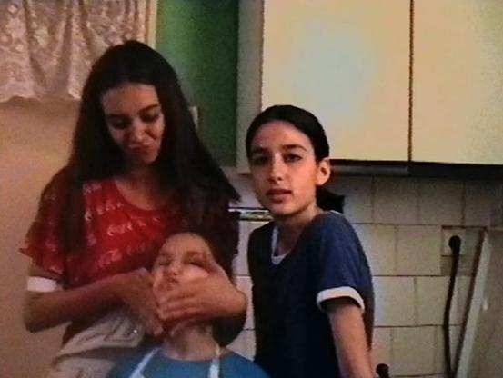 Three young girls shot in Hi8. One is pulling a younger girl's chin into a funny face. The third girl looks towards the camera. From 78 Days.