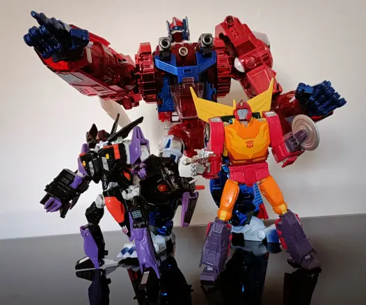 Primal Prime (TransArt's Flame Guardian) in the background points dramatically at something over the heads of tje smaller Skywarp (Beast Machines Botcon exclusive) and  Rodimus (Studio Series '86 Movie Hot Rod), both ready for battle. Rodimus has deployed his circular blade saw.