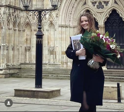 Kirsty Ryder, standing in front of the impressive York Minster, holding a bouquet of flowers and her thesis. She looks overjoyed.