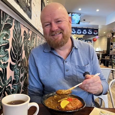 Ray smiling across the table from me, using his chopsticks to pull a chunk of pork from his bowl of pork cutlet curry udon.