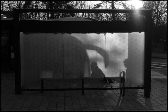Black and white film photo. The shadows of boarding passengers are shown on the frozen glass wall of the bus stop.