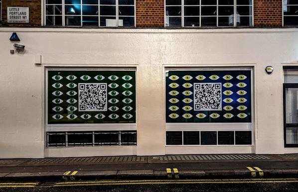Two large windows on a street have QR codes surrounded by regularly shaped eyes.