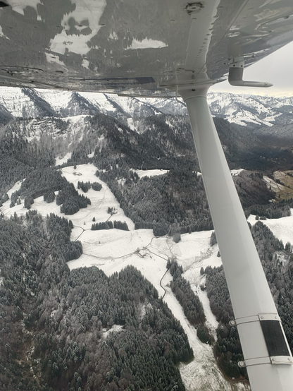 View out of a cockpit window. Alps. Some snow. Wing strut of a high wing plane.