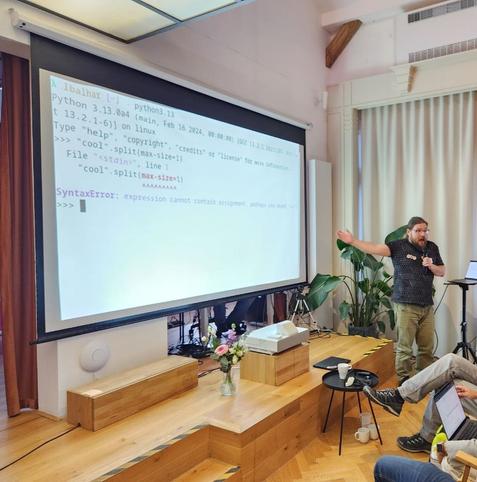 Me in front of presentation screen. A Python 3.13 traceback is depicted, with colorized output, a new feature of Python 3.13.