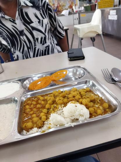 a thali (metal mess plate) with rice + channa dal (chickpea curry), yoghurt and sweets in the langgar (community kitchen) of the neighbourhood gurdwara (Sikh temple).