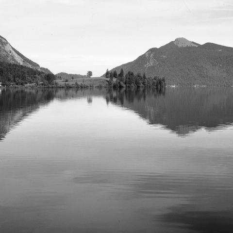 Monochrome photo of two mountain peaks reflected in water at the bottom.