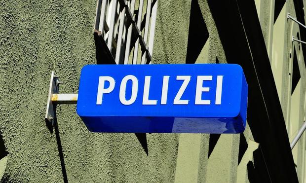 Blaues Schild an eine Hauswand mit vergitterten Fenster geschraubt, mit der Aufschrift Polizei