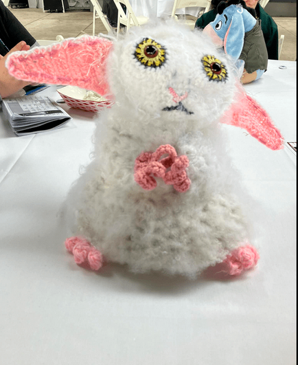 A crocheted white figure with large yellow eyes, wide pointy pink ears, pink hands and pink toes; its surface is mostly fluffy, made by combing the yarn. It's about 12 inches tall.