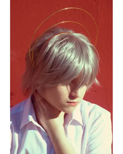 Cosplay de Kaworu Nagisa. Aparezco ante un fondo rojo de torso hacia arriba sujetando mi cuello con una pose un poco religiosa al llevar un halo simulando un ángel.