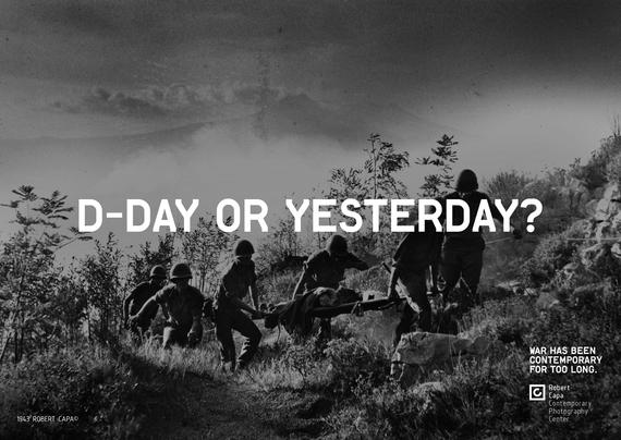A black and white photo with centered text that reads "D-DAY OR YESTERDAY?". The photo shows a group of soldiers carrying a wounded person up a hill.