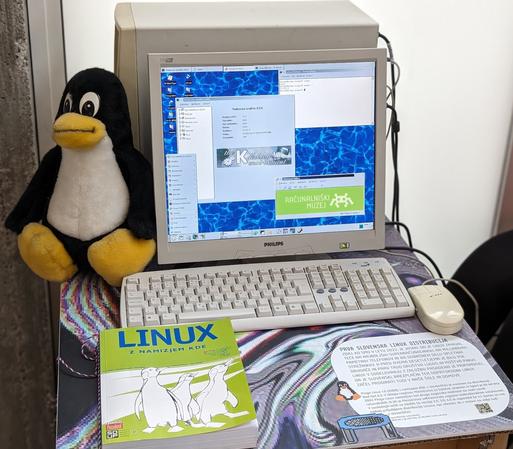 Stari namizni računalnik v ozadju, pred njim pa monitor LCD na katerem se vidi staro namizno okolje KDE 1.1.2, ki teče na slovenski GNU/Linux distribuciji Pingo iz leta 2000. Odprto je okno Nadzornega središča KDE, meni za zaganjanje programov, terminalski program Konsole in program urejevalnika Advanced Editor, v katerem je na na svetlo zelenem ozadju bel napis »Računalniški muzej« z logotipom na desni, Levo od monitorja je postavljena plišasta igrača pingvin. Pred monitorjem je stara tipkovnica in zraven računalniška miška. Pred tipkovnico je tiskana izdaja knjige LINUX z namizjem KDE založbe Pasadena.

Avtor fotografije: Računalniški muzej