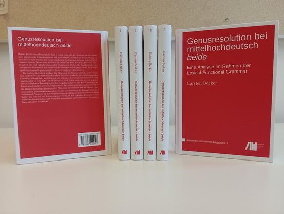 Rückseite, vier Bücher mit Buchrücken und Vorderseite des Buches auf einem leeren Schreibtisch vor Korkpinnwand