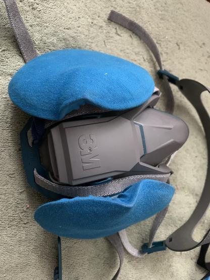 A 3M 6500 series quick-latch respirator with P100 filters. The lurid magenta-coloured filters are tastefully obscured with blue cotton jersey fabric slipcovers which do not impede breathing.