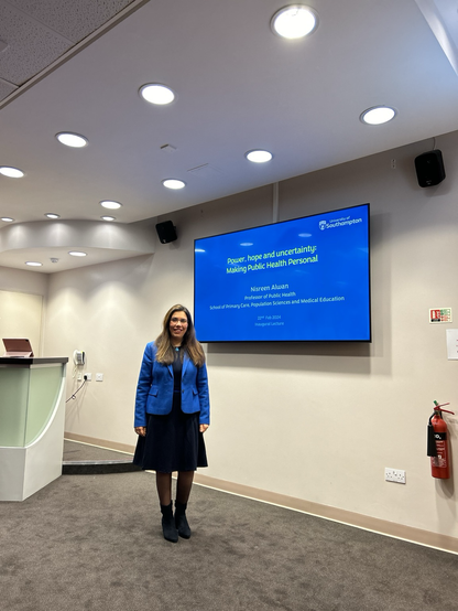 Me standing in front of the screen showing the title slide from my inaugural lecture: power hope and uncertainty: making public health personal.