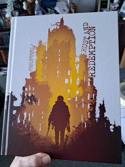 Image showing the front cover of the Rust and Redemption book from Monte Cook Games. The cover image features a silhouetted figure against a ruined building coloured in shades of yellow, orange and brown against a white backdrop.